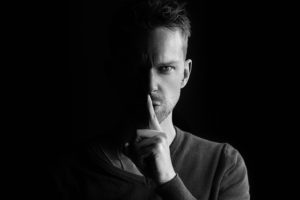 man holding finger to lips to keep a secret - Dan Moisand discusses how to avoid financial scams