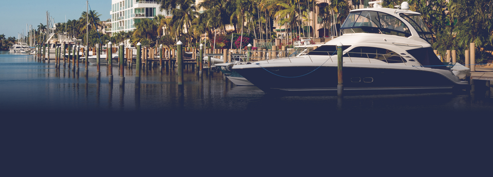 This is a photograph of a luxury boat docked in canal waters behind a residential building surrounded with palm trees by Las Olas in Fort Lauderdale, Florida.